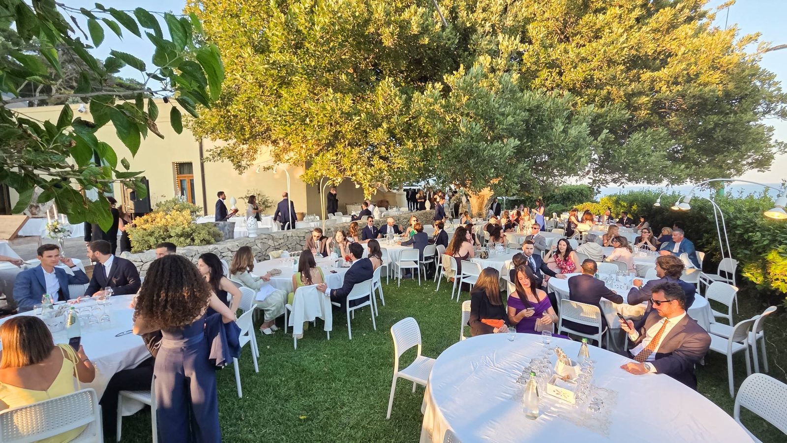 Ricevimento nel giardino di Cala dei Balcani al tramonto, con gli ospiti ai tavoli all'ombra degli alberi — Santa Cesarea Terme, Salento
