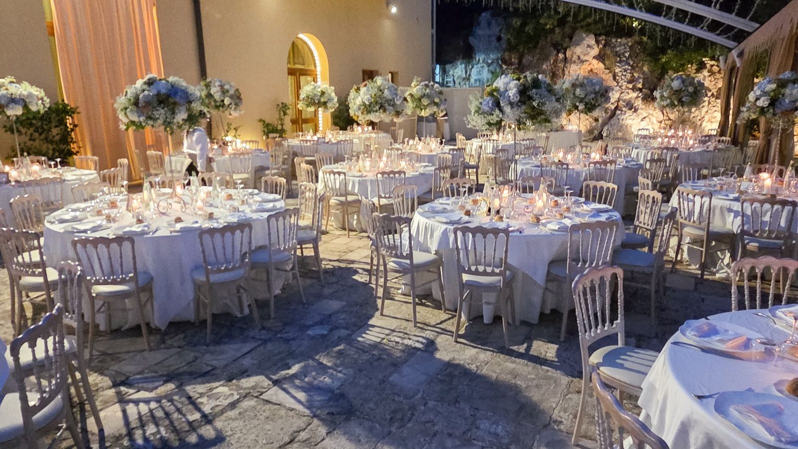 Cena serale nel cortile in pietra con alte composizioni di ortensie azzurre e candele accese — Cala dei Balcani, Santa Cesarea Terme