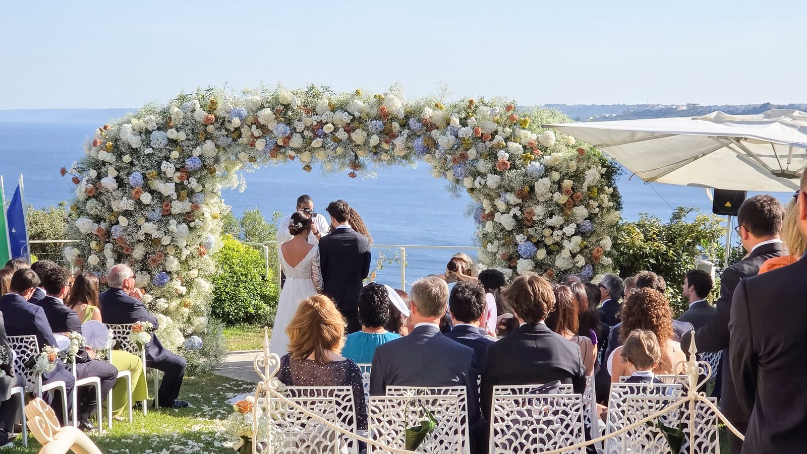 Cerimonia di matrimonio davanti all'arco floreale circolare affacciato sul mare Adriatico, con gli ospiti seduti — Cala dei Balcani, Salento