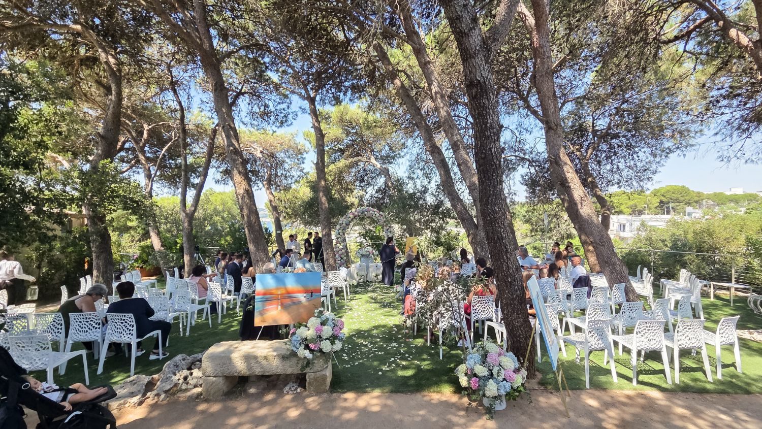 Cerimonia all'aperto nella pineta di Cala dei Balcani, con arco floreale e sedie bianche tra i pini — Santa Cesarea Terme, Salento