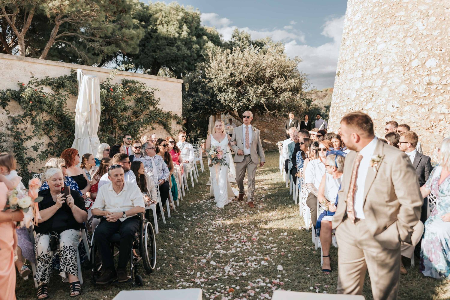 Les invités étrangers le long de l&rsquo;allée et le marié qui attend la mariée, la tour sarrasine en arrière-plan &mdash; Cala dei Balcani, Salento