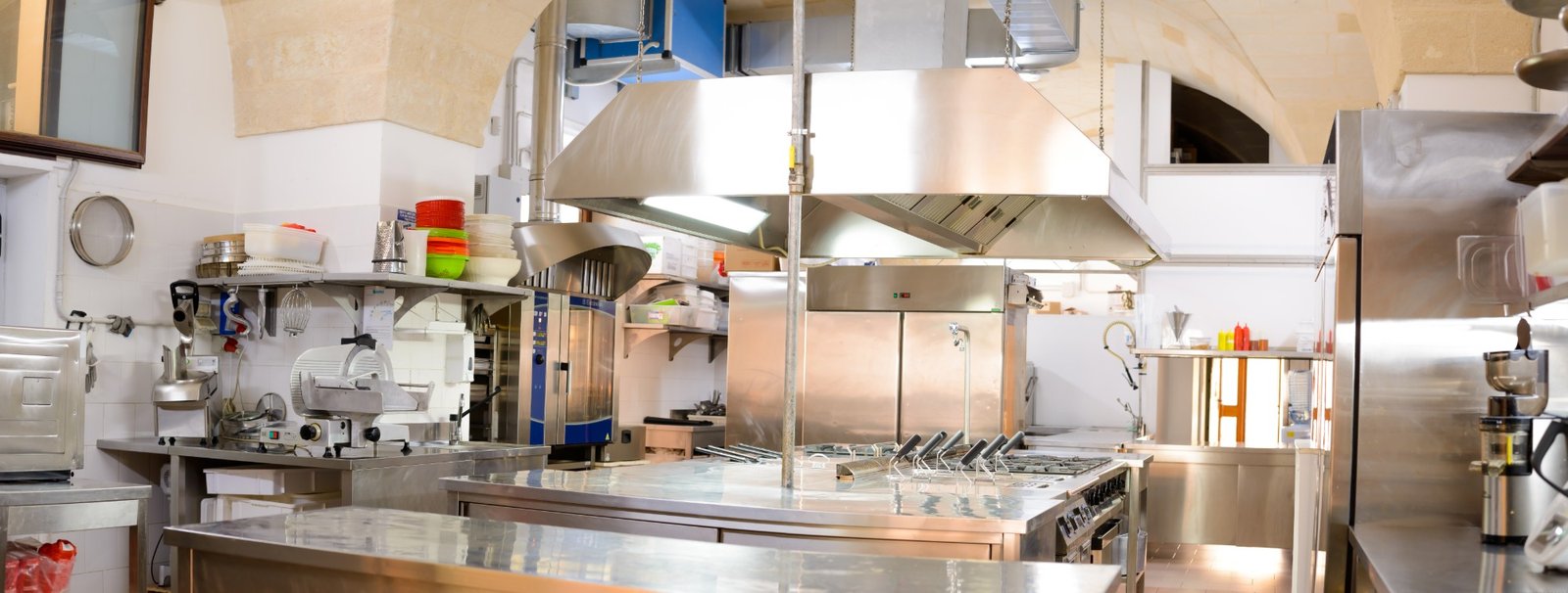 La cucina professionale di Cala dei Balcani sotto le volte in pietra: laboratorio in acciaio con forno a convezione, affettatrice e fuochi a vista, dove i menù dei matrimoni sono preparati espressi — Santa Cesarea Terme, Salento