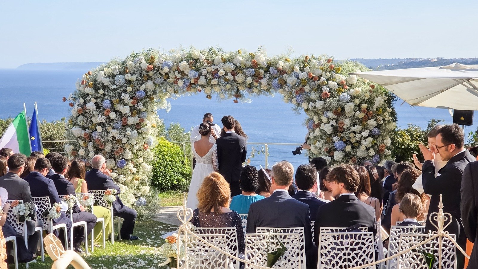 Sposi sotto l'arco floreale durante la cerimonia nuziale all'aperto con vista mare — Cala dei Balcani, Santa Cesarea Terme, Salento