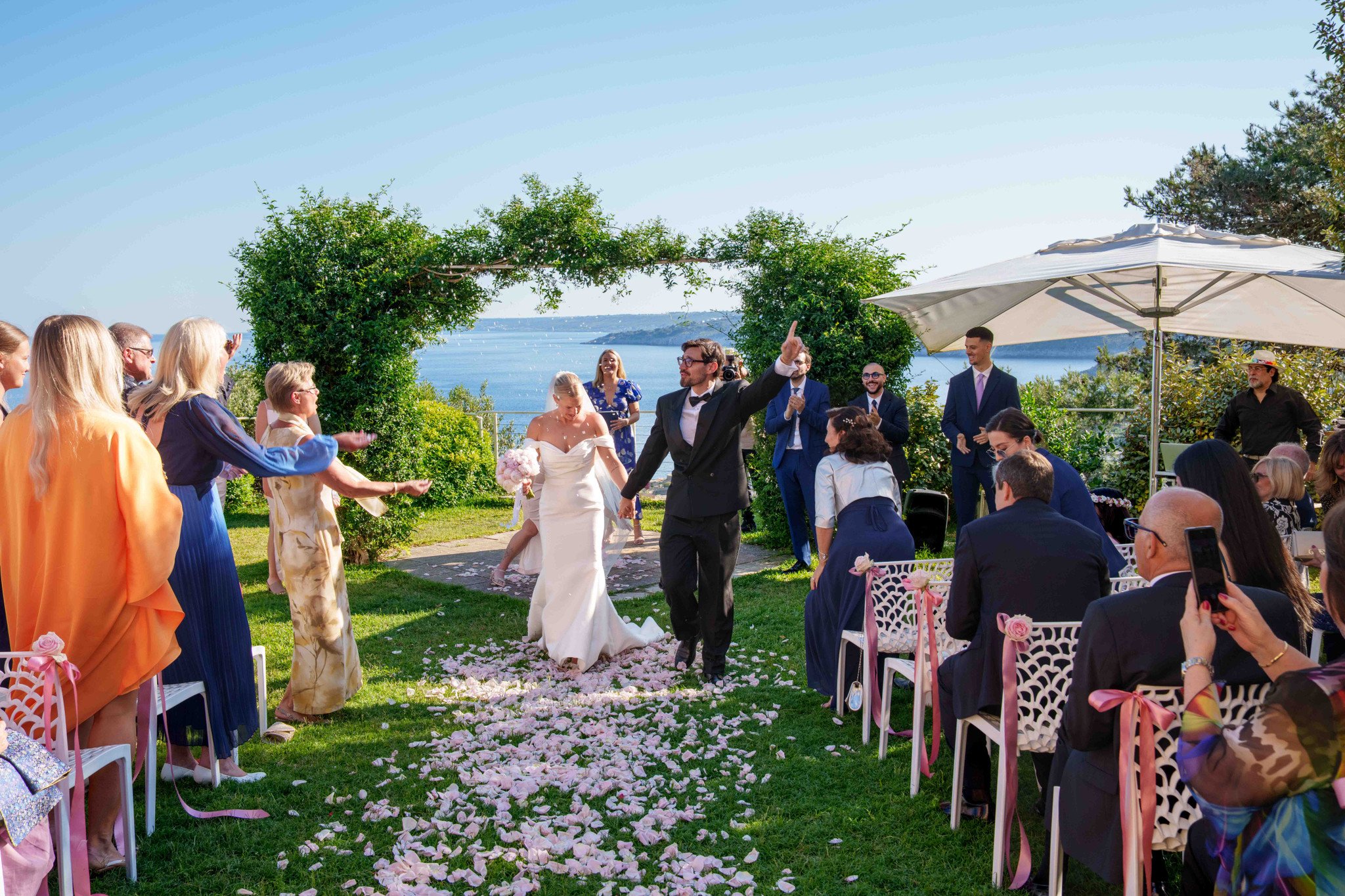 Sposi che escono dalla cerimonia accolti dagli ospiti esultanti — matrimonio internazionale a Cala dei Balcani, Santa Cesarea Terme, Salento