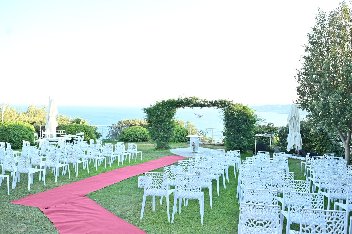 The ceremony area with its floral arch and red carpet above the sea
