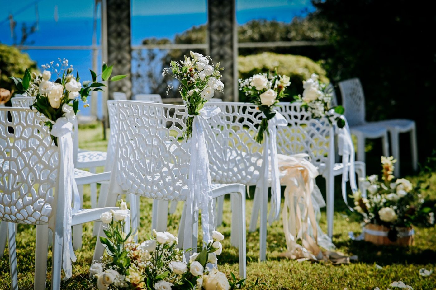 Chaises de cérémonie ornées de roses blanches et de rubans de lin, la mer en arrière-plan &mdash; Cala dei Balcani, Salento