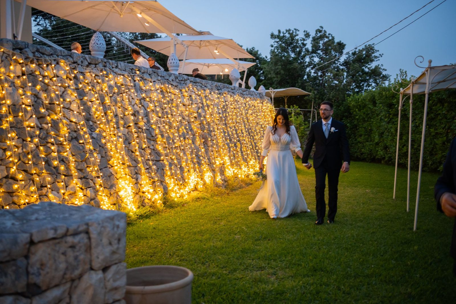 Sposi nel giardino di Cala dei Balcani al tramonto, lungo il muro a secco illuminato da luci calde — Santa Cesarea Terme, Salento