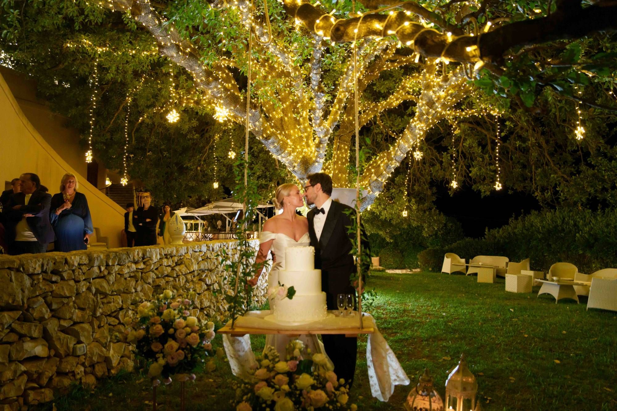 Gli sposi davanti alla torta nuziale sotto la quercia secolare illuminata — matrimonio a Cala dei Balcani, Santa Cesarea Terme, Salento