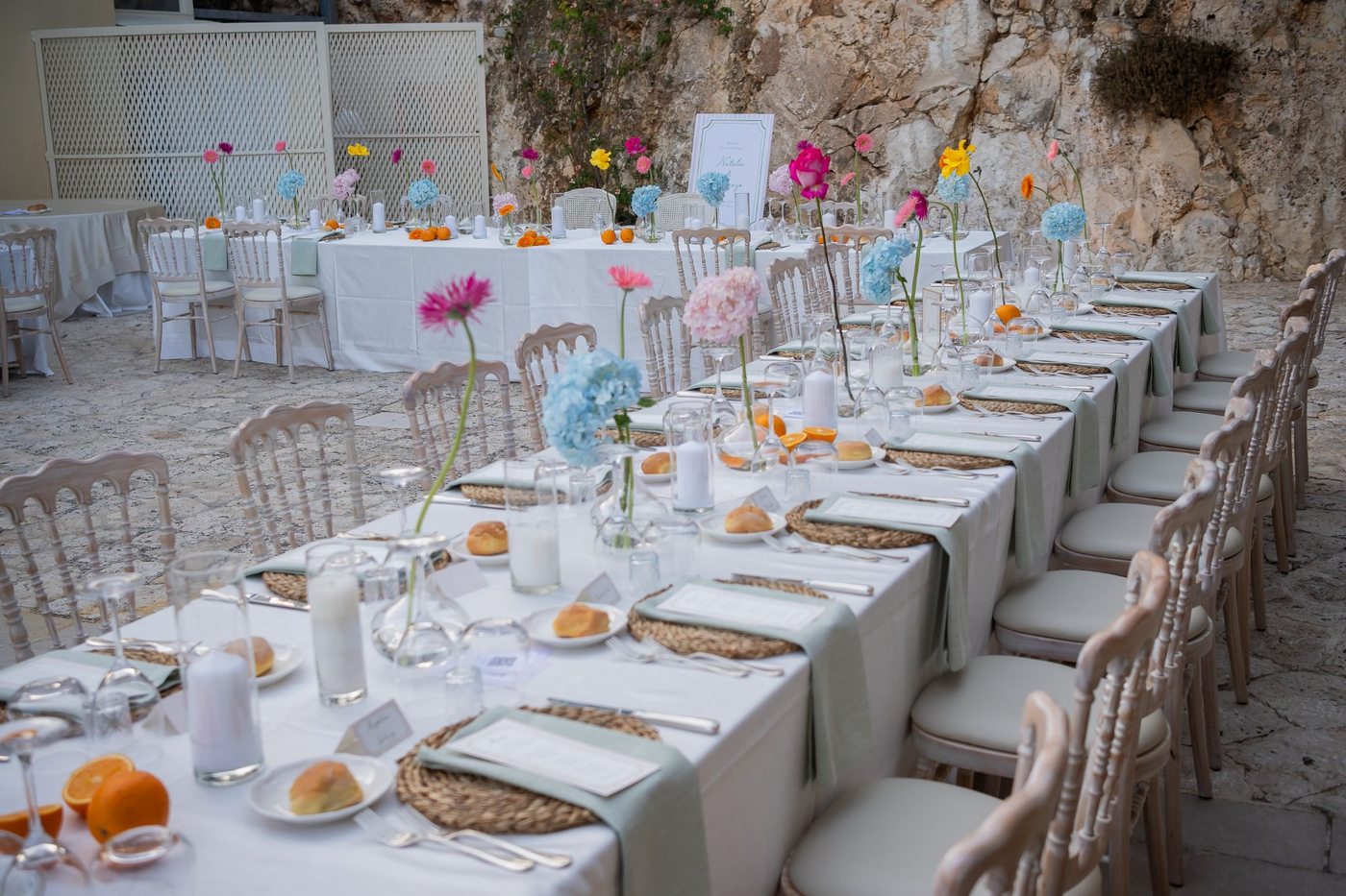 Les tables d&rsquo;une réception intime avec gerberas colorés, hortensias et oranges, la table des mariés en arrière-plan &mdash; Cala dei Balcani, Salento